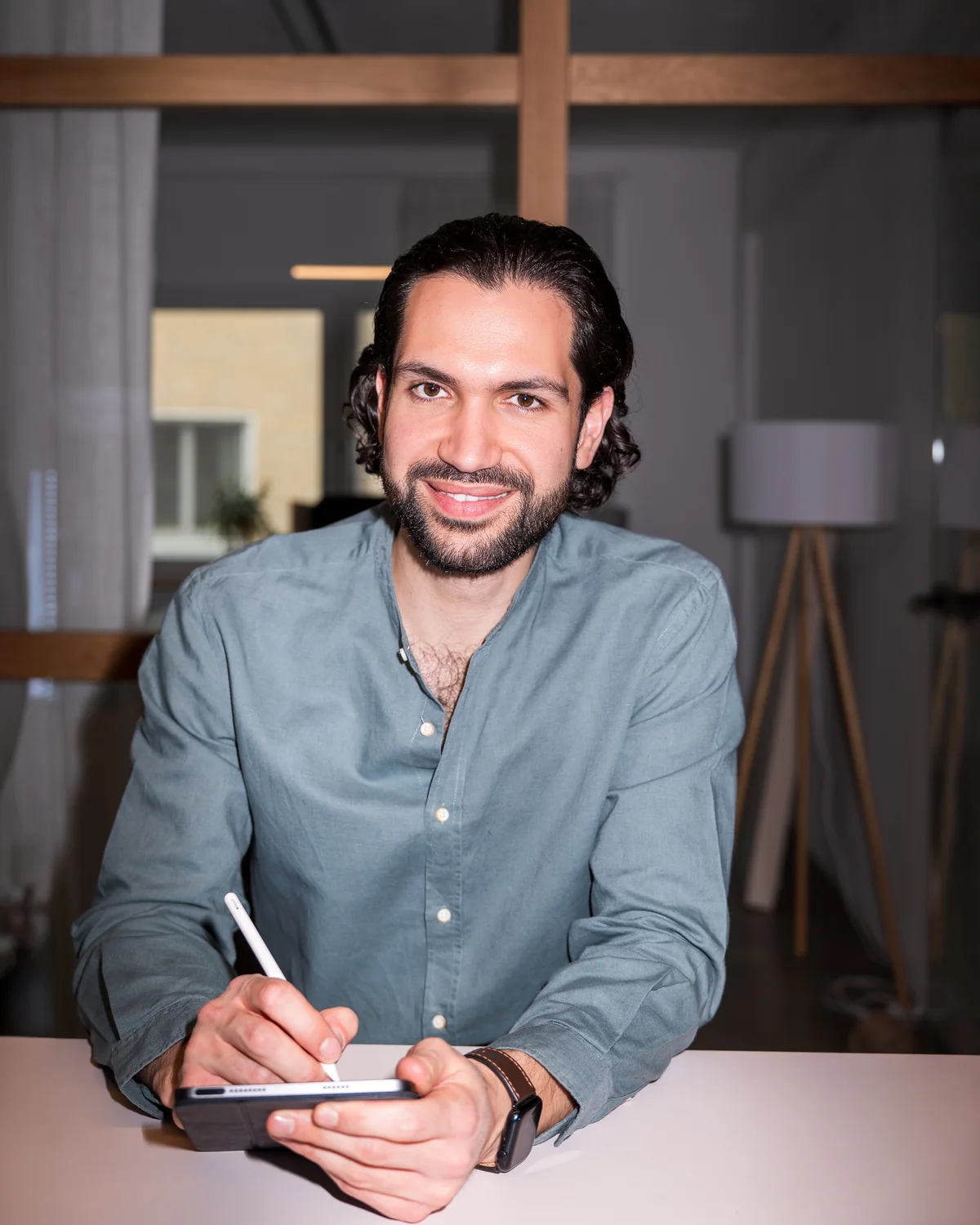 Joti Fotiadis am Tisch mit Tablet und Stift, mit Blick zur Kamera