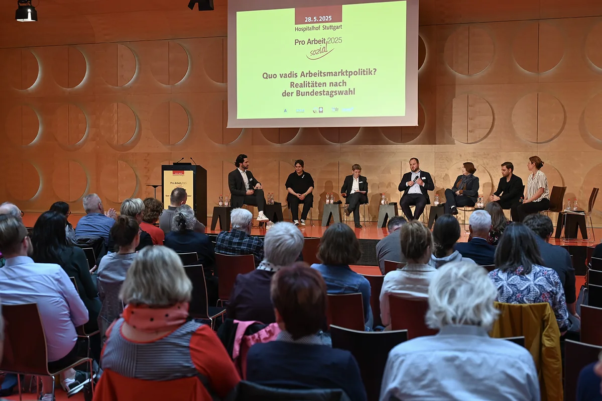 Joti Fotiadis mit sechs Gesprächsgästen auf der Bühne bei Pro Arbeit sozial
