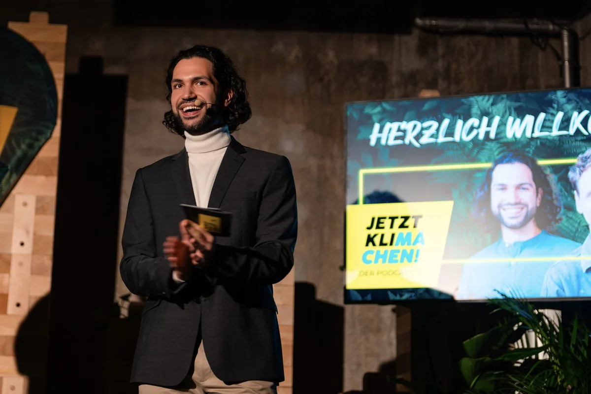Joti Fotiadis mit Headset vor dem Jetztklimachen-Podcastmotiv